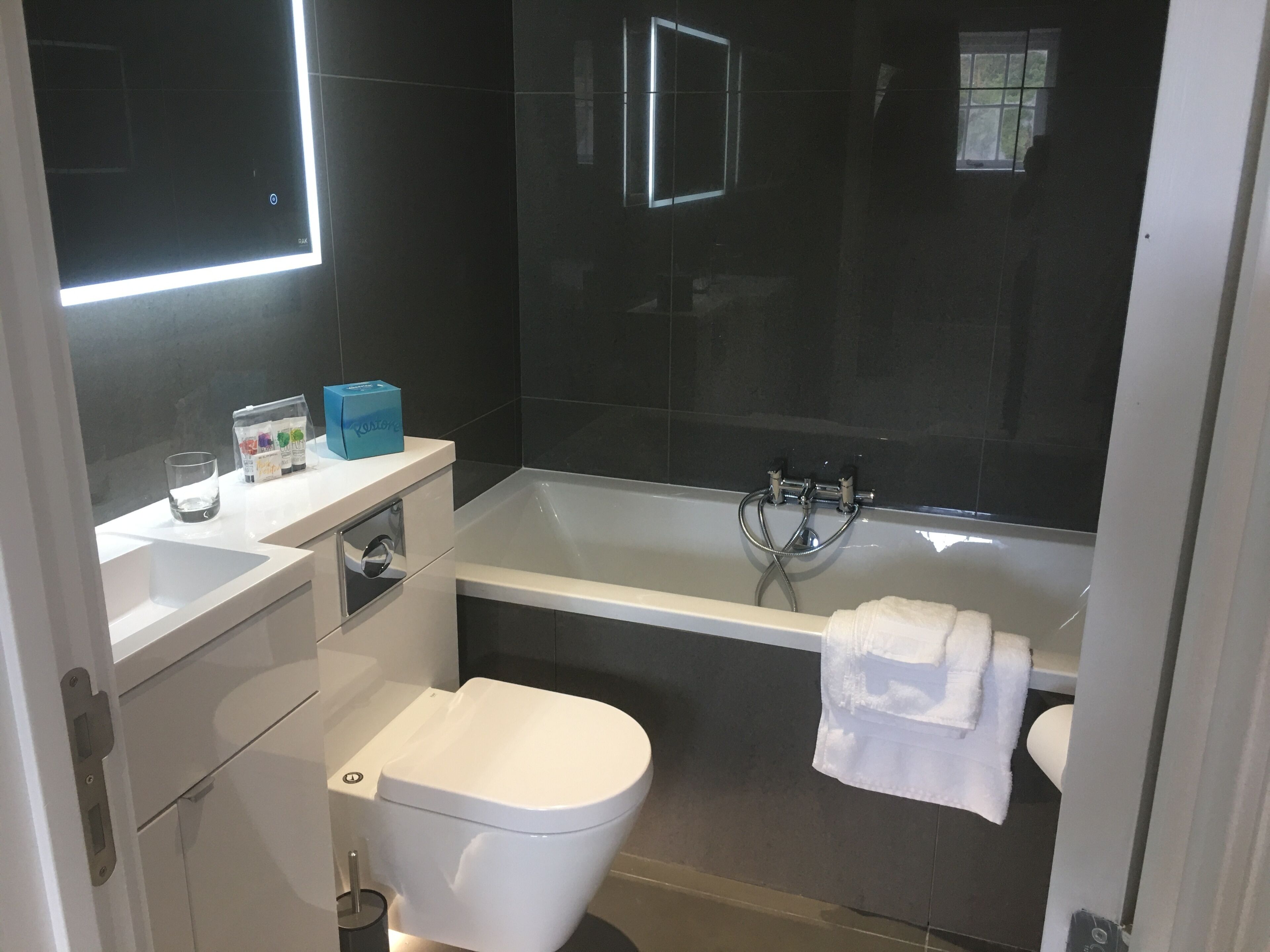 A modern bathroom with a white toilet, a bathtub with a towel, and a mirror above the sink.
