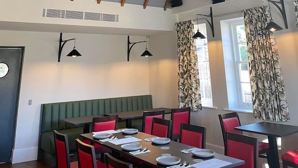 A dining area with a high ceiling, wooden beams, and a hanging ship decoration. Tables are set with plates and cutlery.