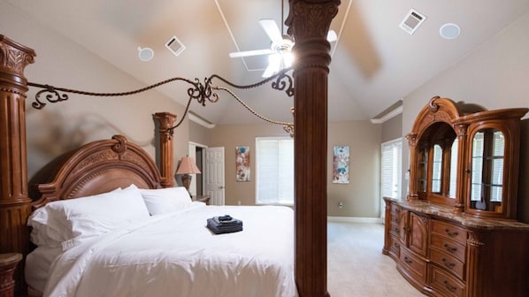 Een ruime slaapkamer met een groot bed, een houten dressoir en een plafondventilator.