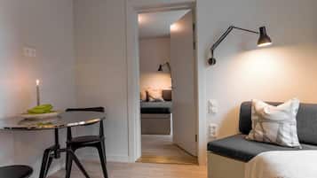 A modern bedroom with a bed, a bedside table with a lamp, a small table with a candle and bananas, and a sofa with a blanket.