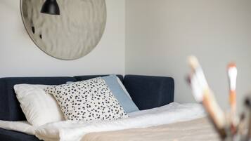 A modern bedroom with a dark blue sofa, a round mirror, and a bedside table with a lamp.