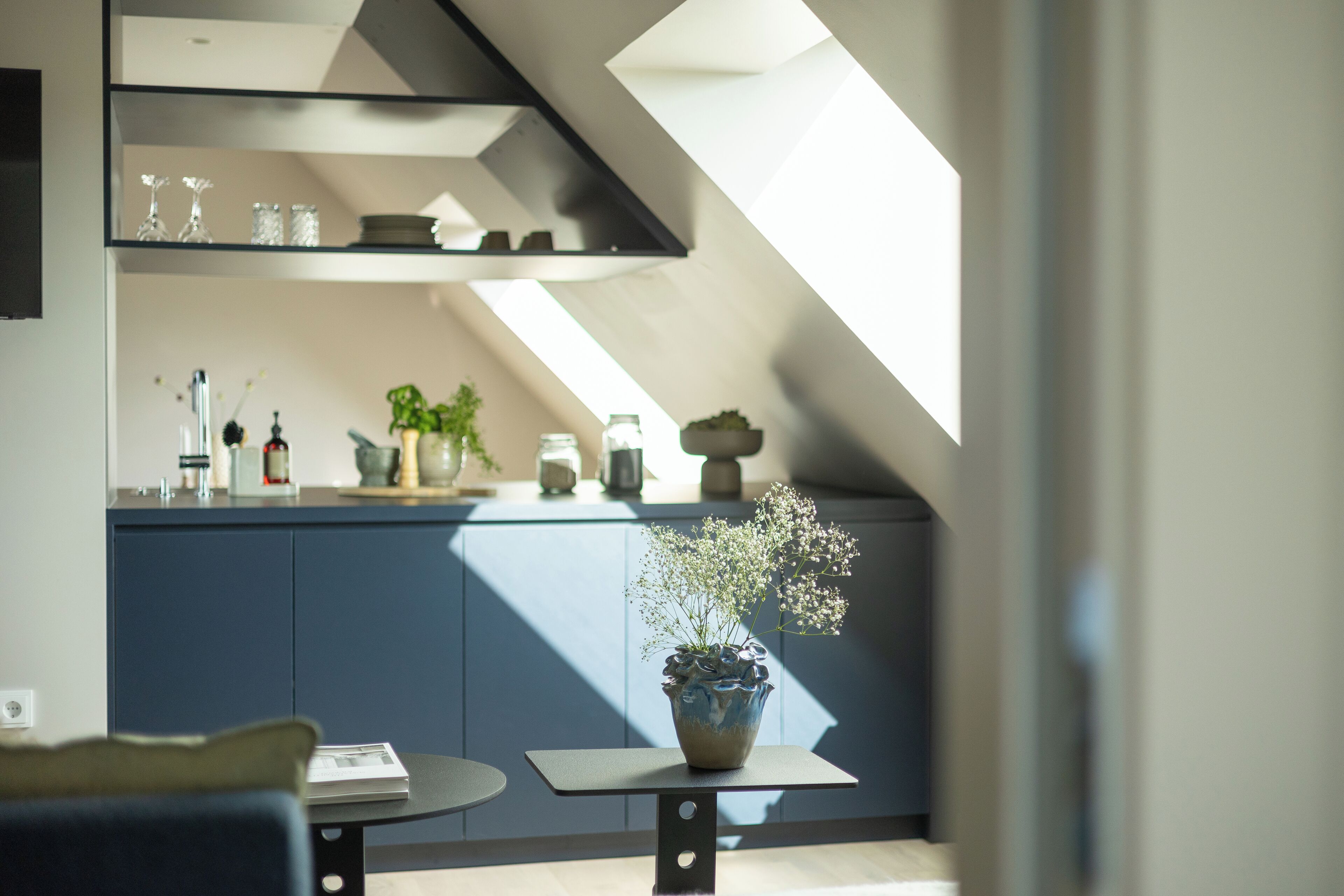 A modern kitchen with a skylight, a dining area with a table and chairs, and a potted plant on a small table.