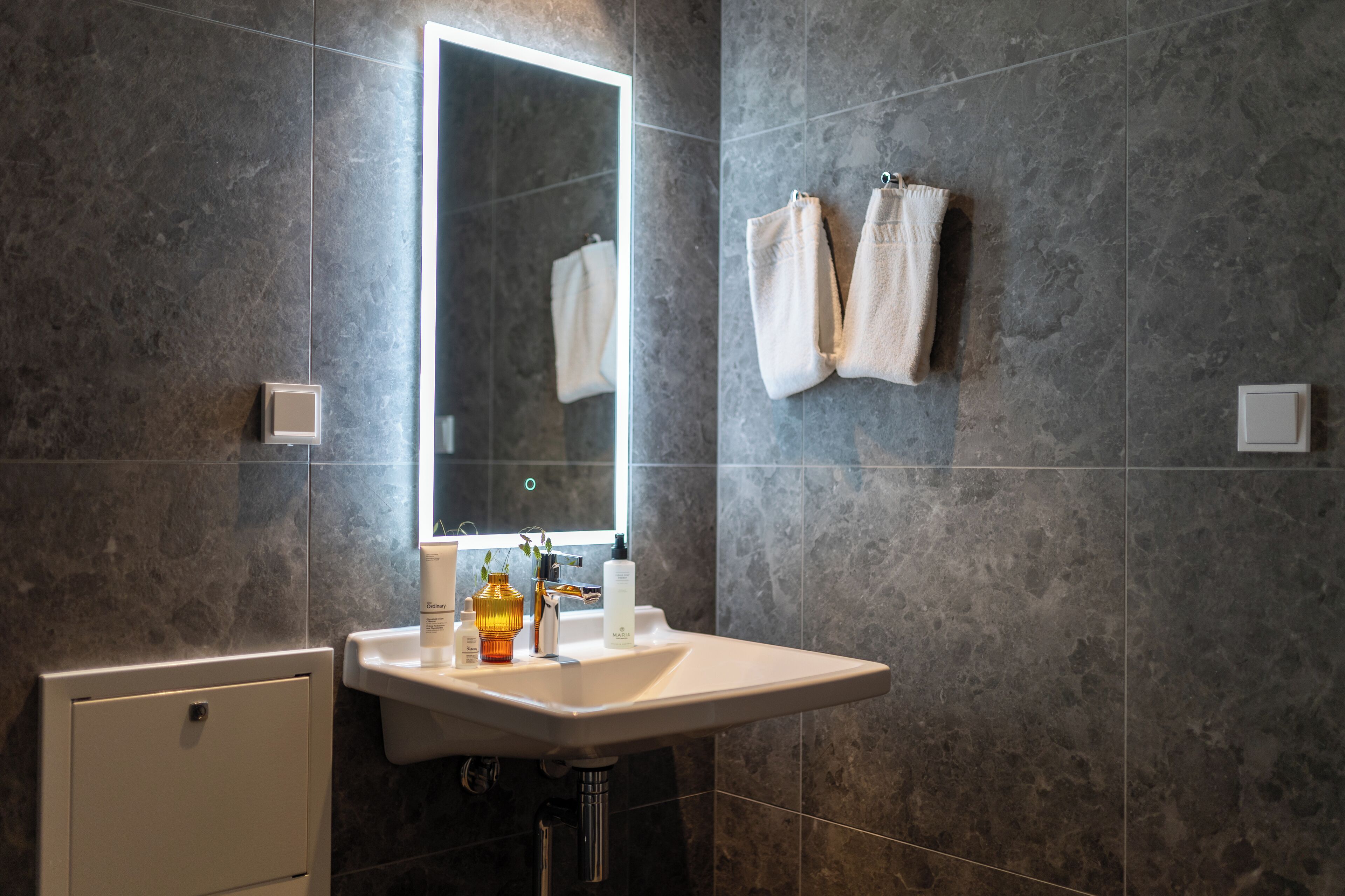 A bathroom with a white sink, a mirror, and two towels hanging on the wall.