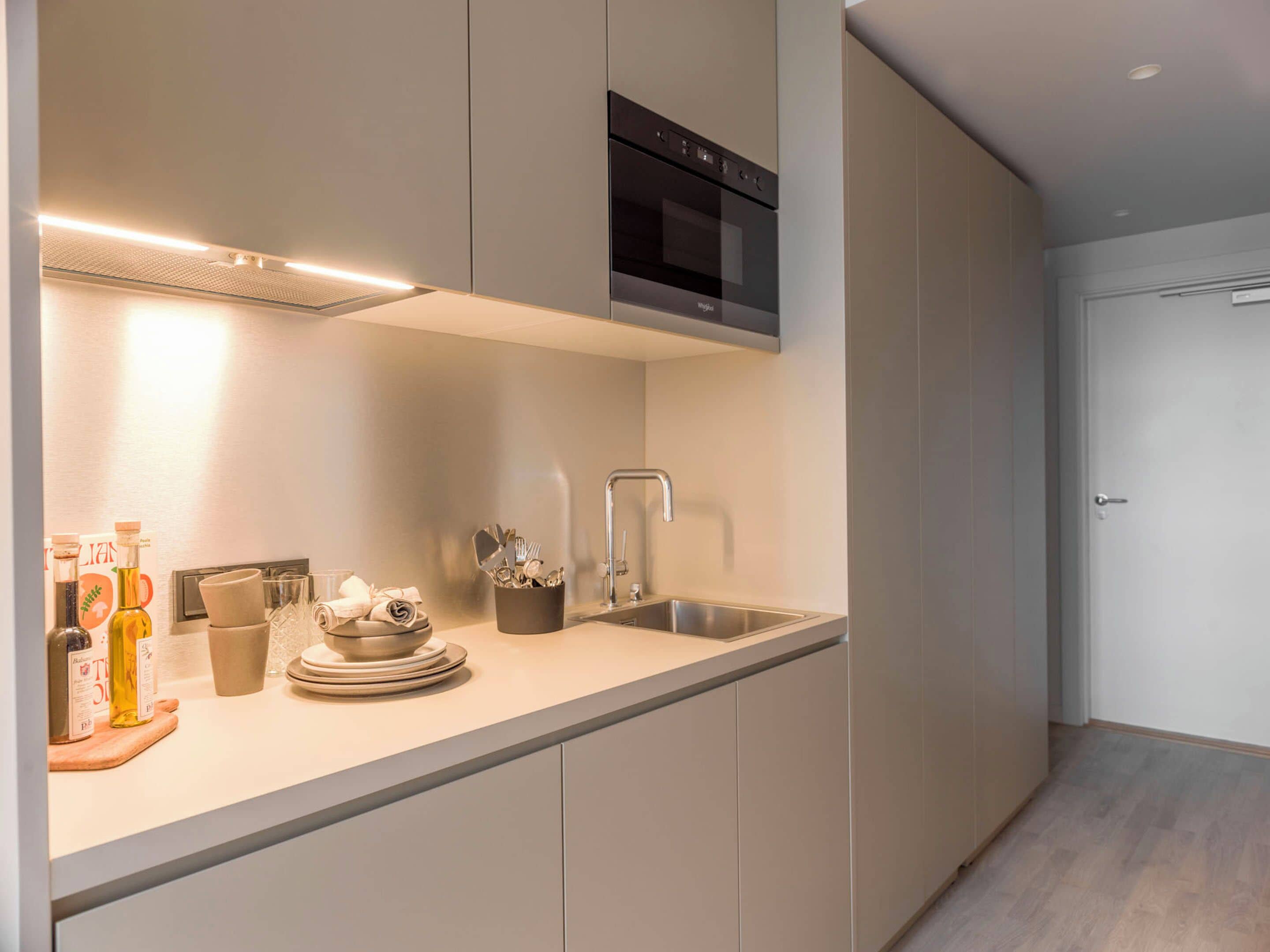 A modern kitchen with a built-in oven, stainless steel sink, and a countertop with various kitchen items.