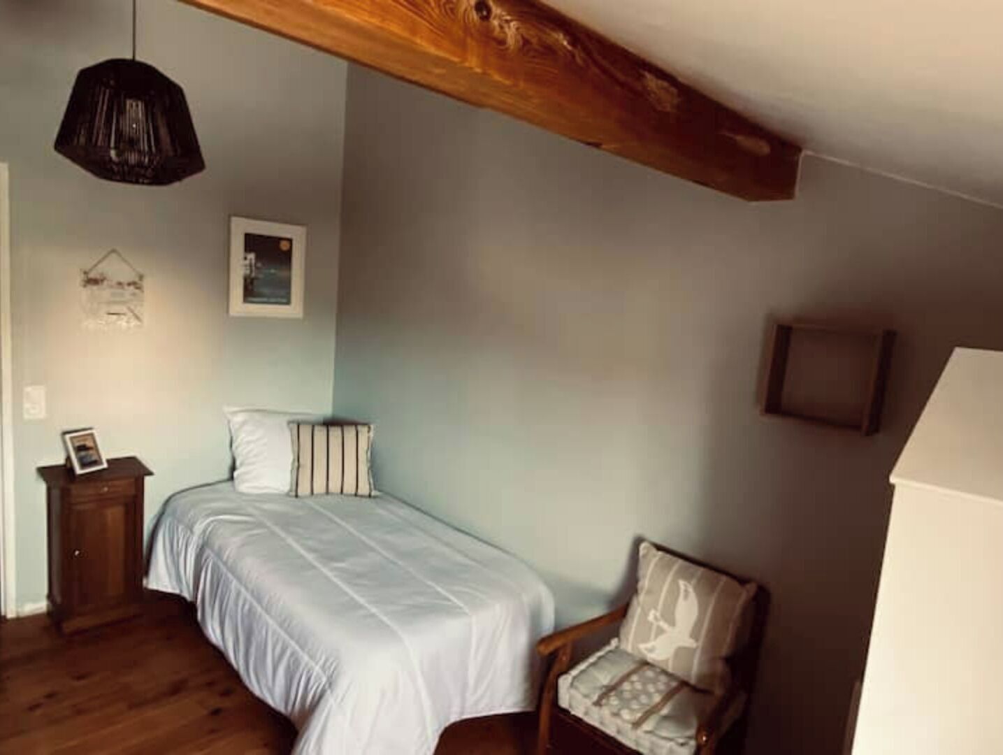 Un dormitorio con cama, una silla, una lámpara colgante y un cuadro en la pared.