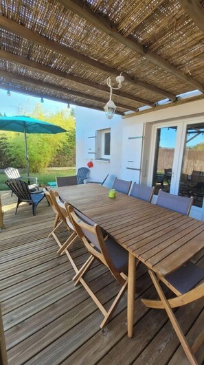 Un patio al aire libre con una mesa y sillas de madera, un farol colgante y vistas al jardín trasero.