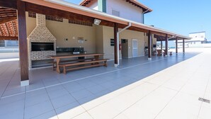 An outdoor patio area with a brick fireplace, wooden benches, and a covered seating area. - Raridade - Apt próx praia vista mar ar con (Ubatuba)