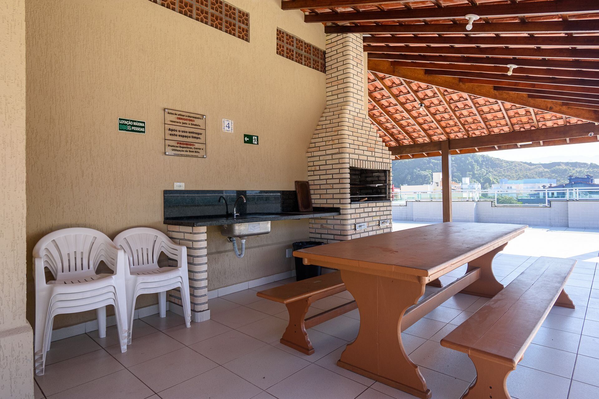 An outdoor patio with a brick oven, two white plastic chairs, and a wooden table.