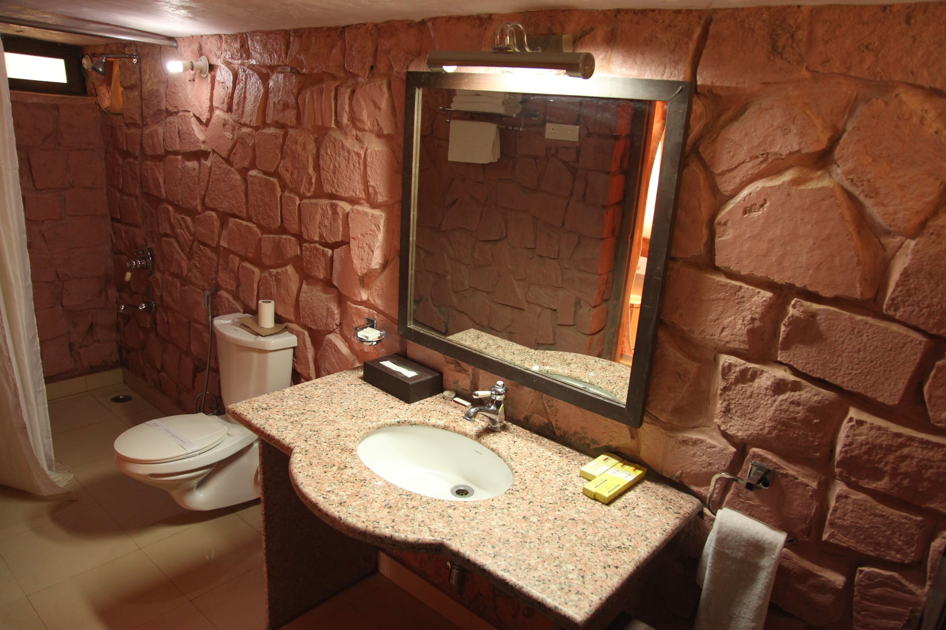 A bathroom with a stone wall, a sink, a mirror, and a toilet.