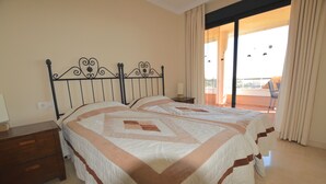 A bedroom with two beds, a wooden nightstand, and a view of the outdoors through a sliding glass door. - Sun Hill Los Pacos 2 Bed Apt (Fuengirola)