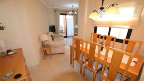 A dining area with a wooden table and chairs, a sofa, a TV, and a lamp. - Sun Hill Los Pacos 2 Bed Apt (Fuengirola)