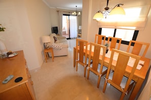 A dining area with a wooden table and chairs, a sofa, a TV, and a lamp.