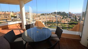 A balcony with a glass wall, a round table, and wicker chairs. - Sun Hill Los Pacos 2 Bed Apt (Fuengirola)
