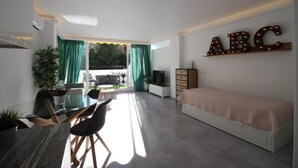 A modern living room with a glass dining table, a sofa, and a bed. There is a TV and a dresser. The room has a large window with curtains. - Walking Distance to beach Torreblanca Rio Sol (Fuengirola)