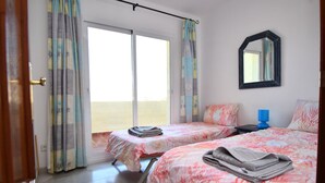 A hotel room with two beds, a sliding glass door to the balcony, a bedside table with a lamp, and a mirror on the wall. - Seaviews Balcones de Chaparral 3 Bed Apt (Mijas Costa)