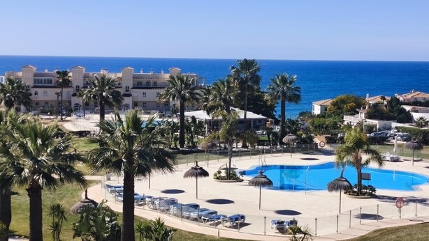 A resort with a central pool, palm trees, and a view of the sea. - Seaviews Balcones de Chaparral 3 Bed Apt (Mijas Costa)
