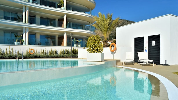 Un hôtel moderne doté d’une piscine, d’un espace extérieur aménagé et d’un bâtiment blanc aux volets noirs.