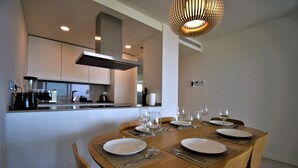 Un espace repas moderne avec une table ronde en bois, dressée pour six personnes, et agrémentée d’assiettes, de couverts et de verres à vin.