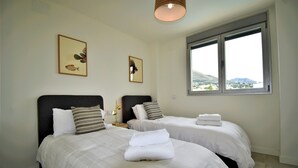 Une chambre d’hôtel avec deux lits, du linge de lit blanc, des oreillers à rayures et des œuvres d’art accrochées aux murs.