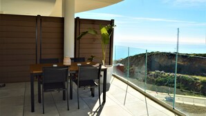 Un balcon avec une table et des chaises pour prendre les repas, un pot de fleurs et une vue sur une falaise et la mer.