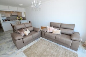Ein Wohnzimmer mit Ecksofa, einer Chandelier und einer Küche im Hintergrund.