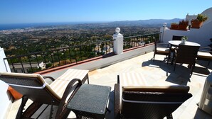 A terrace with wicker furniture, a white balustrade, and a view of a coastal landscape. - Mirador De Mijas  Penthouse Apt Blq 2 (Mijas Pueblo)