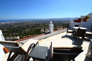 Una terrazza con mobili in vimini, un parapetto bianco e vista su un paesaggio costiero.
