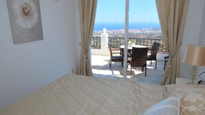 A bedroom with a large bed, a view of the city through a balcony, and a table with chairs outside. - Mirador De Mijas  Penthouse Apt Blq 2 (Mijas Pueblo)