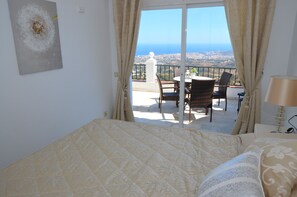 Una camera da letto con un letto grande, vista sulla città da un balcone e un tavolo con sedie all'esterno.
