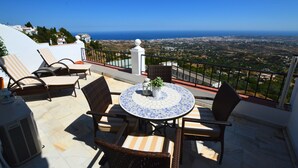 A terrace with wicker chairs and a tiled table, overlooking a coastal landscape. - Mirador De Mijas  Penthouse Apt Blq 2 (Mijas Pueblo)