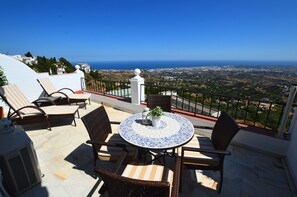 Una terrazza con sedie in vimini e un tavolo piastrellato, con vista sul paesaggio costiero.