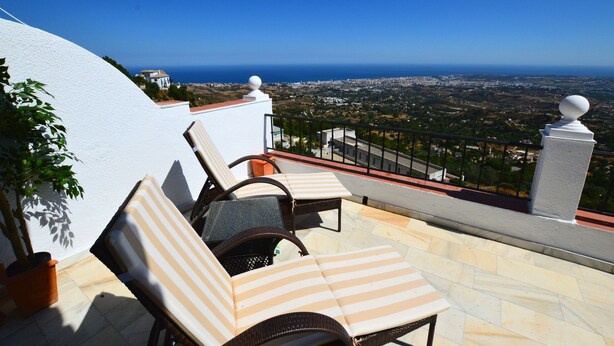 A terrace with two striped lounge chairs, a potted plant, and a view of the coastline. - Mirador De Mijas  Penthouse Apt Blq 2 (Mijas Pueblo)