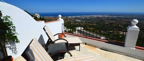 Una terraza con dos sillones reclinables a rayas, una planta en maceta y vistas a la costa.