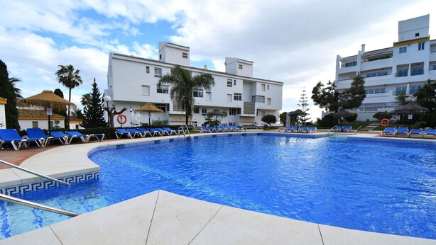 A swimming pool with blue water, surrounded by lounge chairs and palm trees. - Wyndham Resort 4 Bed House (Mijas Costa)