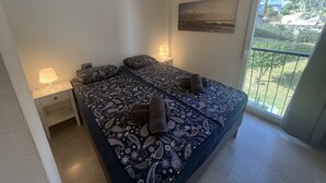 A bedroom with a large bed, two bedside tables with lamps, a ceiling fan, a window with a view of greenery, and an air conditioning unit. - Wyndham Resort 4 Bed House (Mijas Costa)