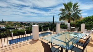 Un balcon avec une table et des chaises en verre, une piscine et une vue sur le paysage urbain.