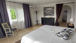 Une chambre à coucher comprenant un lit, une chaise, une commode, un porte-manteau et un tableau accroché au mur.