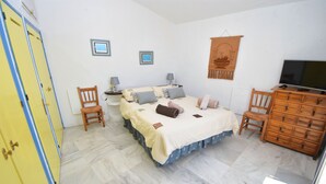 Ein Schlafzimmer mit einem Bett, zwei Stühlen, einem Schminktisch und einem Fernseher. An den Wänden hängen zwei Bilder in Rahmen.