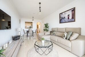 Uma sala de estar moderna com um sofá, uma mesa de centro de vidro e um espaço de jantar com cadeiras.