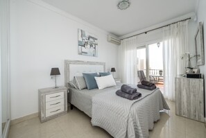 Quarto com cama, mesas de cabeceira, uma cadeira e varanda.