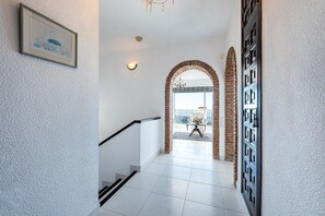 A hallway with white walls, a framed picture, a staircase, and a door with a geometric pattern.