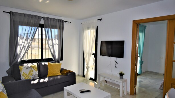 A modern living room with a grey sofa, white coffee table, and a flat-screen TV mounted on the wall. - Pueblo Torrequebrada, Benalmadena 2 Bed Apt (Benalmádena)