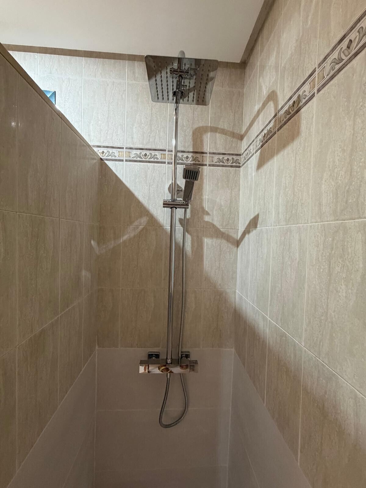 Eine Dusche mit Duschkopf und verstellbaren Bedienelementen an der Wand.