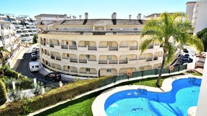 A multi-story building with balconies, a swimming pool, and a road with cars. - Pueblo Torrequebrada, Benalmadena 2 Bed Apt (Benalmádena)