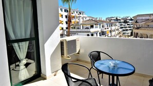 A balcony with a table and chairs, an air conditioning unit, and a view of white buildings with balconies. - Pueblo Torrequebrada, Benalmadena 2 Bed Apt (Benalmádena)