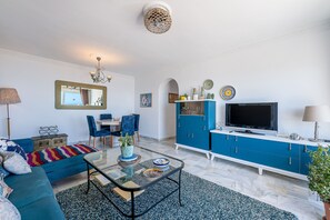 Una sala de estar con sofá, mesa de centro, televisor y armarios azules.