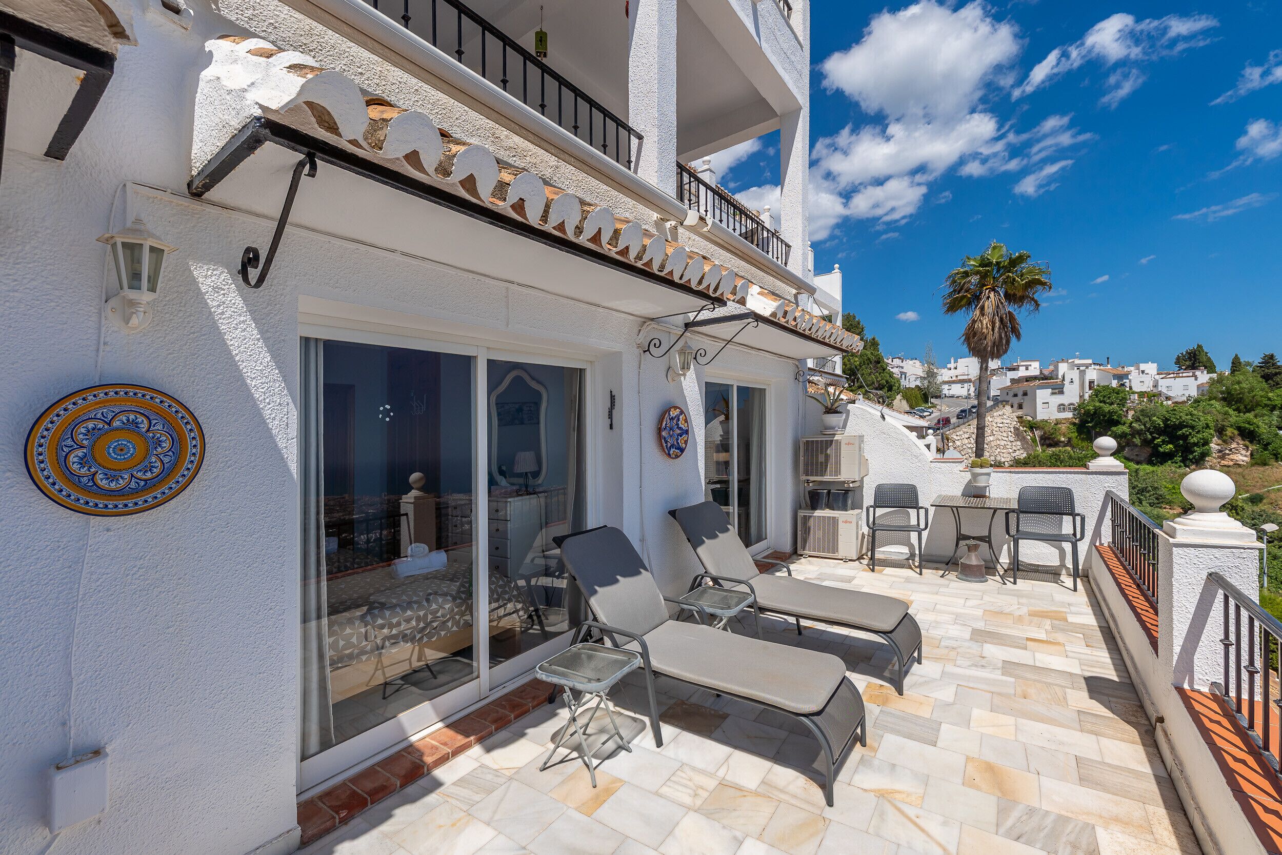 A white building with a balcony, outdoor seating, and a view of a town.