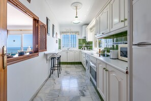 Una cocina con armarios blancos, suelo de mármol, lavadora y vistas al mar.