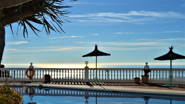 Ein Pool mit freiem Blick auf den Ozean, umgeben von einer weißen Brüstung und Topfpflanzen.