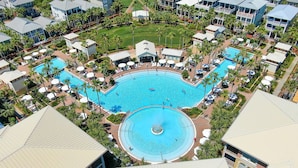A large, circular swimming pool surrounded by palm trees and lounge chairs, with multiple buildings in the background. - Seacrest Beach Home for 19, Huge Pool & Beach Tram + Free Attraction Tickets! (Seacrest Beach)